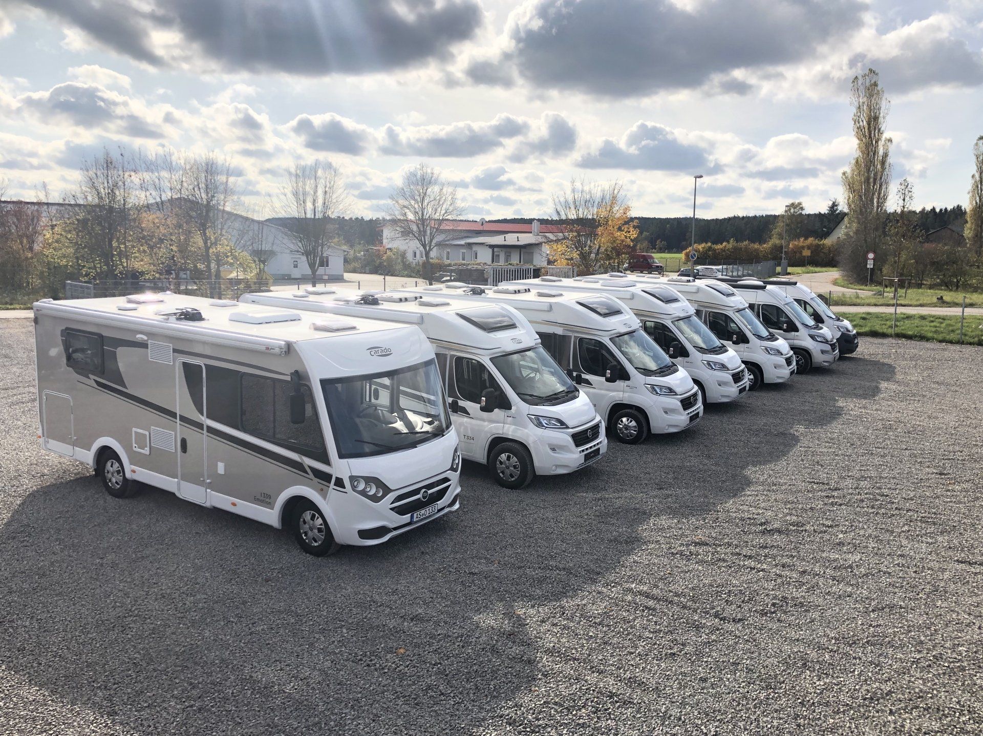 A row of rvs are parked in a gravel lot.