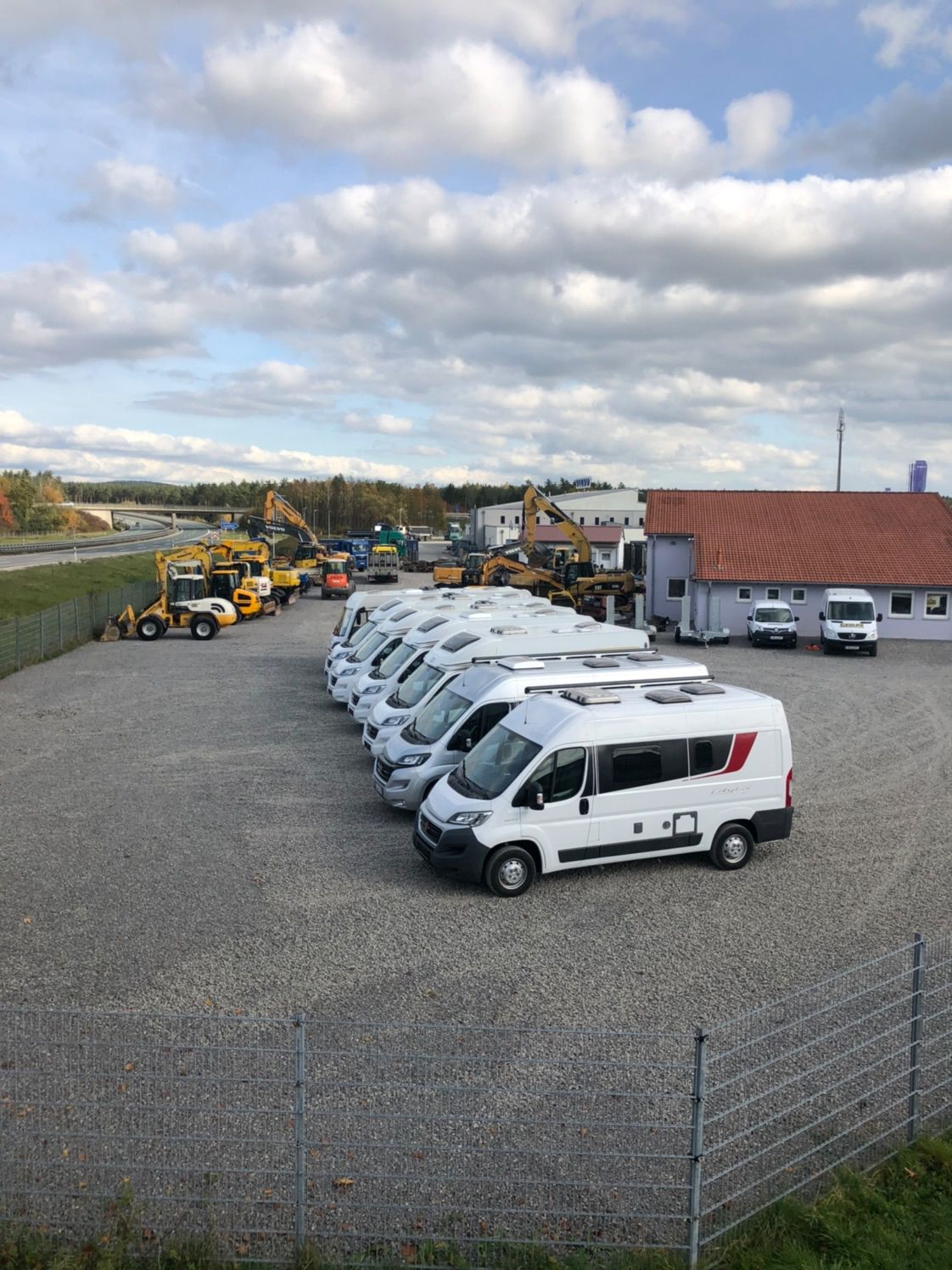 A row of vans are parked in a gravel lot in front of a building.