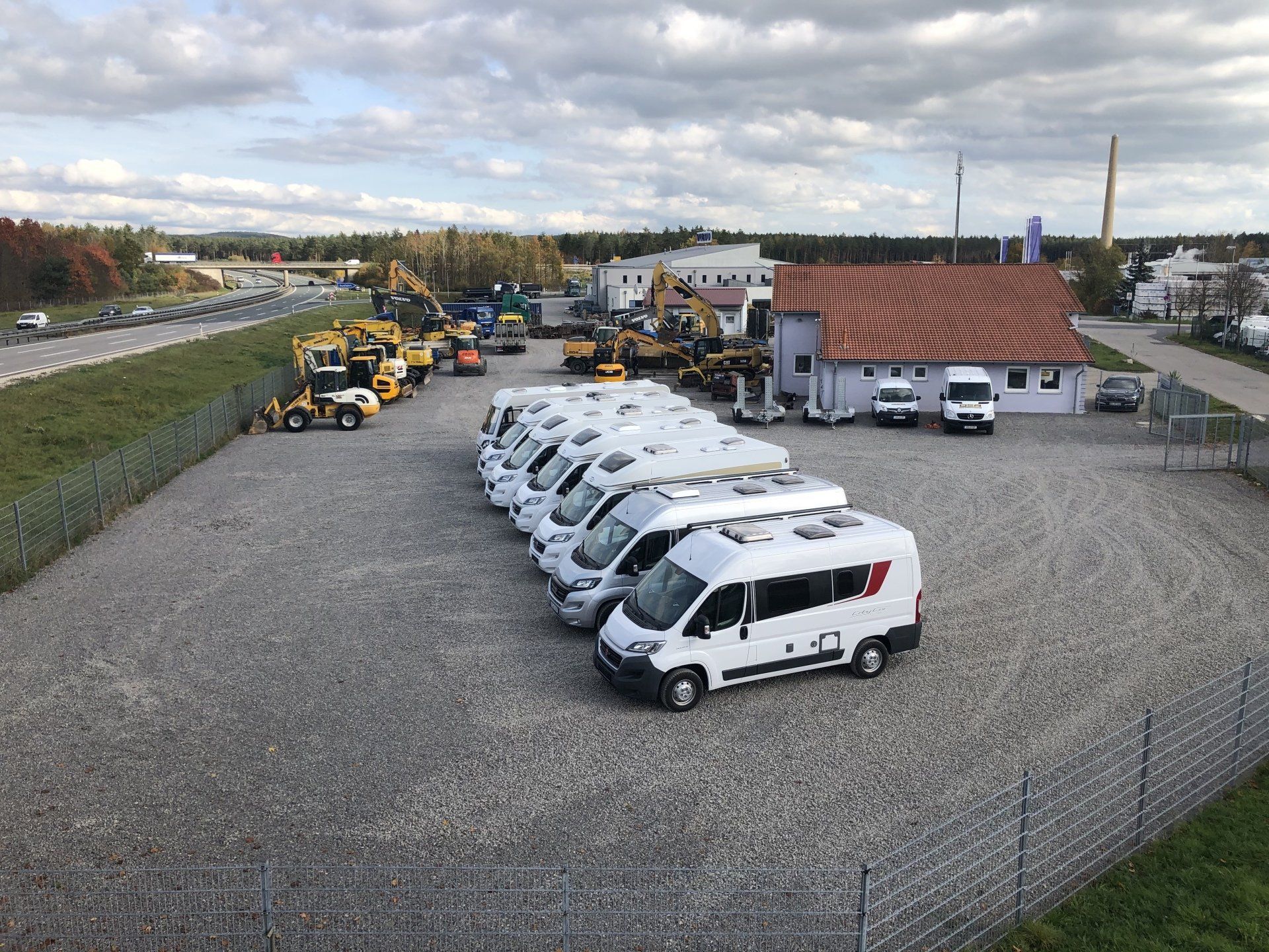 A row of vans are parked in a gravel lot in front of a building.