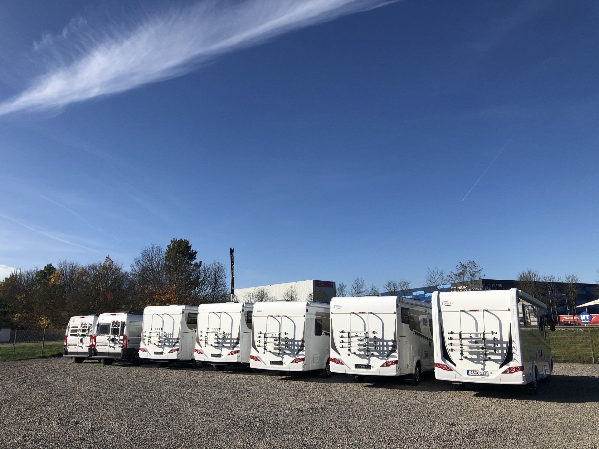 A row of white rvs are parked in a gravel lot.