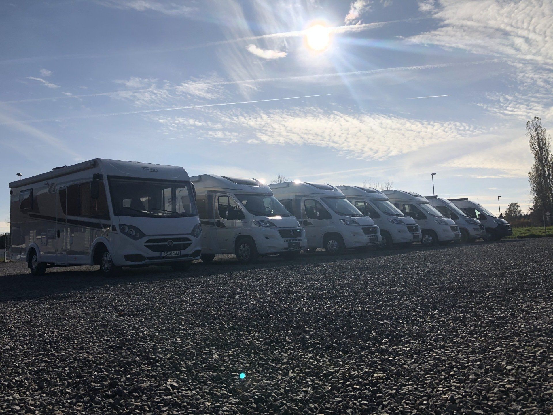 A row of rvs are parked in a gravel lot.