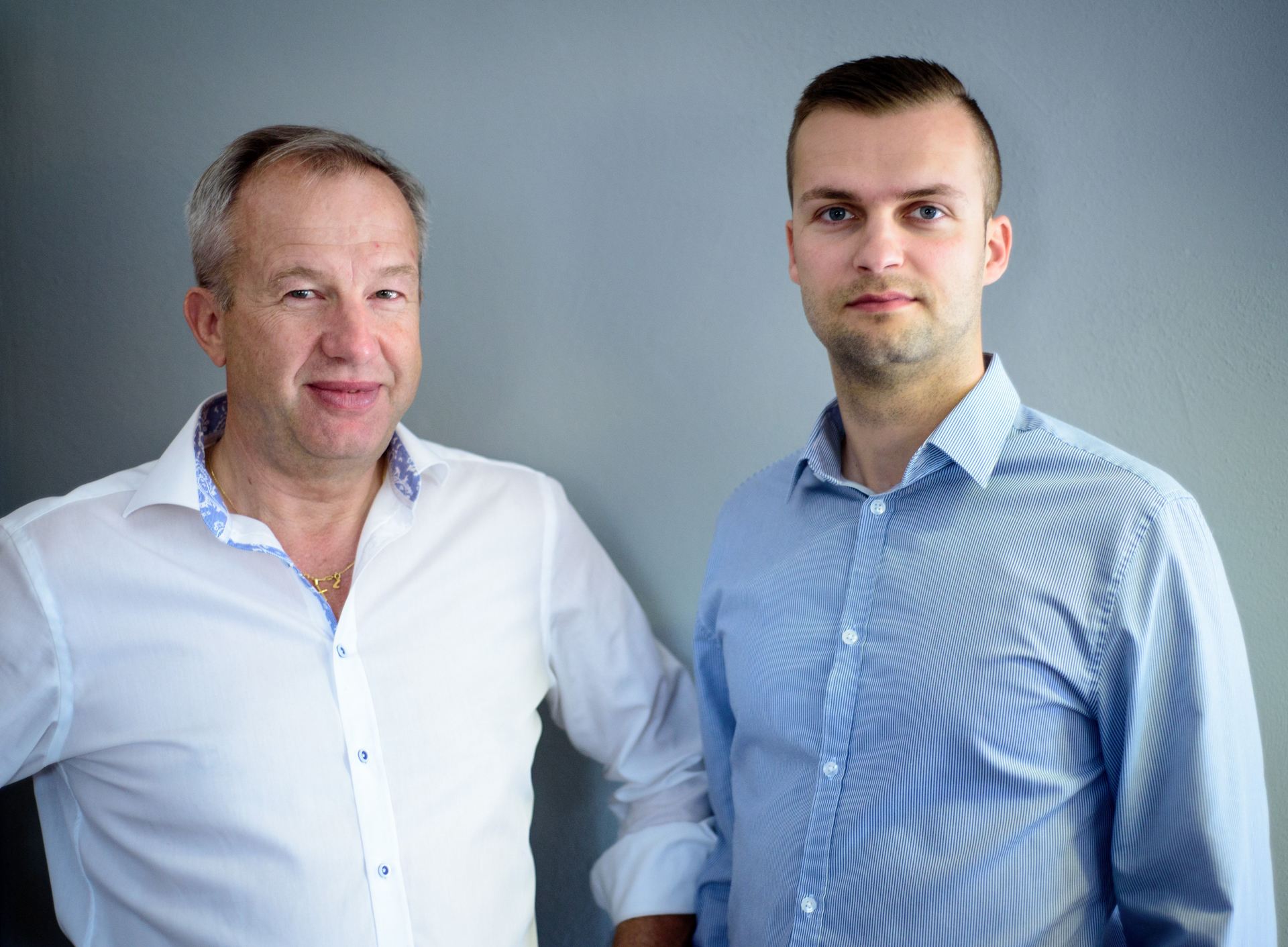 Two men are standing next to each other in front of a wall.