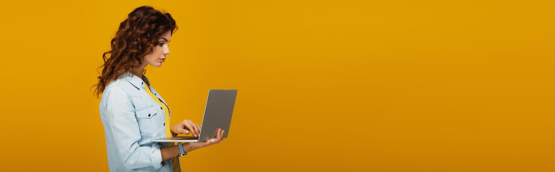 A woman is using a laptop computer on a yellow background.