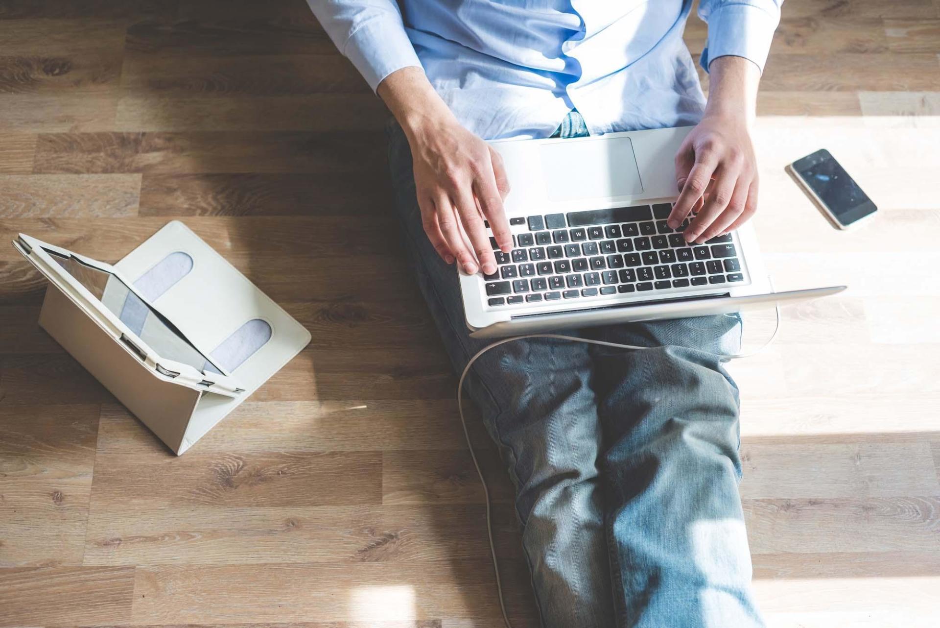 A man is sitting on the floor using a laptop computer.