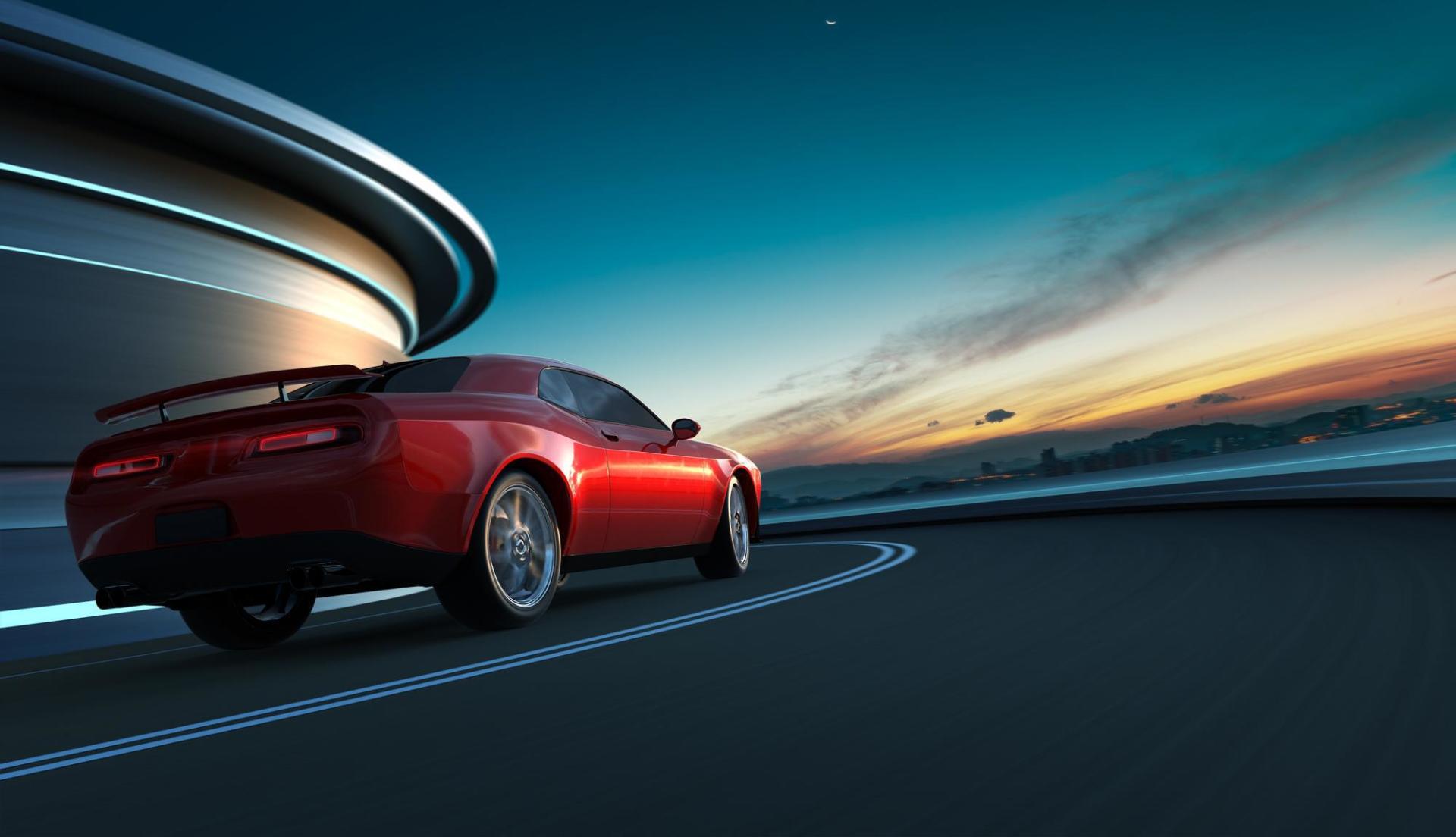 A red sports car is driving down a road next to a building at sunset.