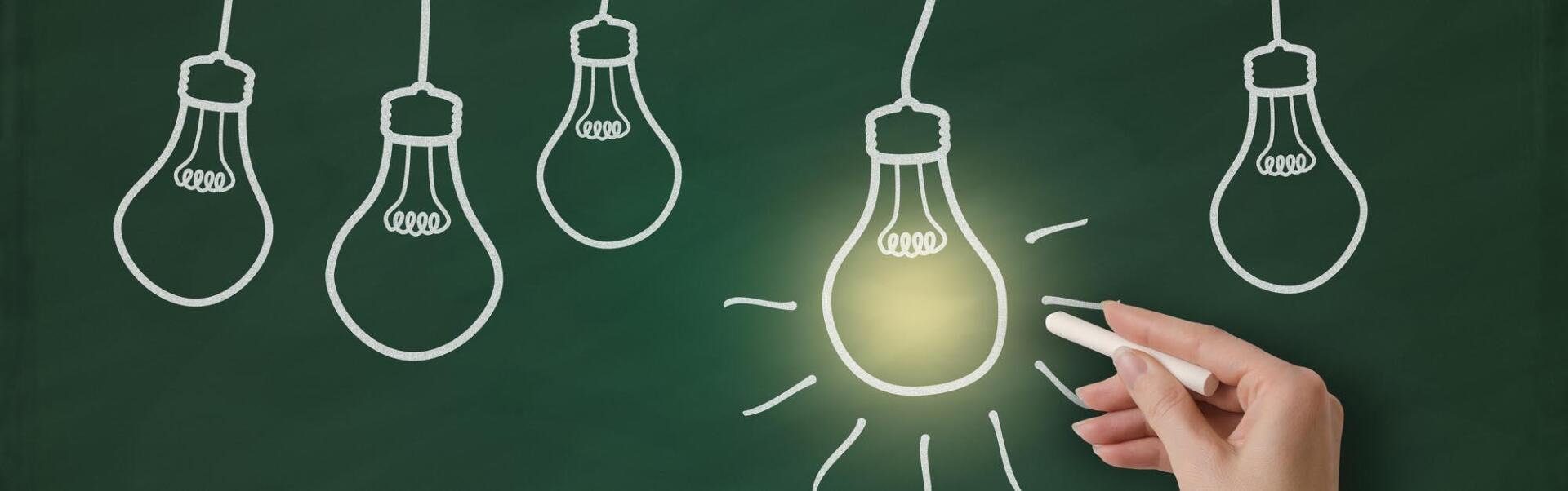 A person is drawing light bulbs on a blackboard with chalk.