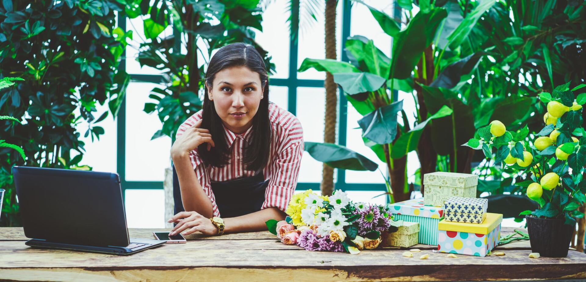 A woman is sitting at a table with a laptop and flowers.