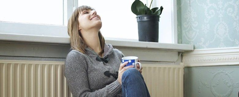 una donna appoggiata a un calorifero con una tazza in mano