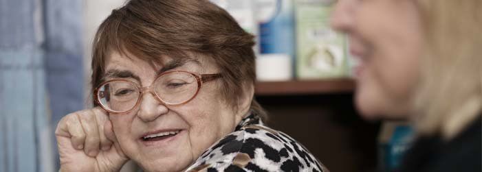 An elderly woman wearing glasses is talking to another woman.