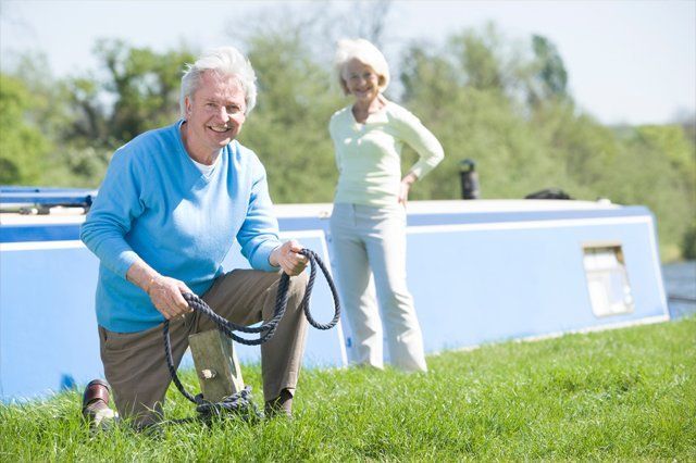 A man is kneeling in the grass holding a leash while a woman stands behind him