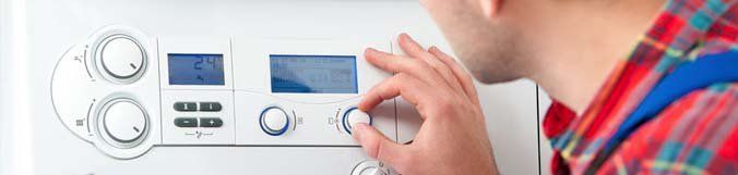 A man is adjusting a thermostat on a boiler.