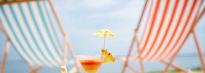 A close up of a cocktail in a glass with an umbrella on a beach.