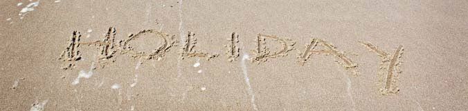 The word holiday is written in the sand on the beach.