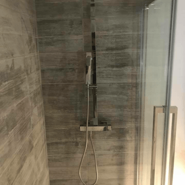 Une cabine de douche avec une pomme de douche et une porte vitrée.