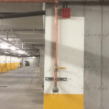 Un tuyau en cuivre est fixé à un mur dans un parking