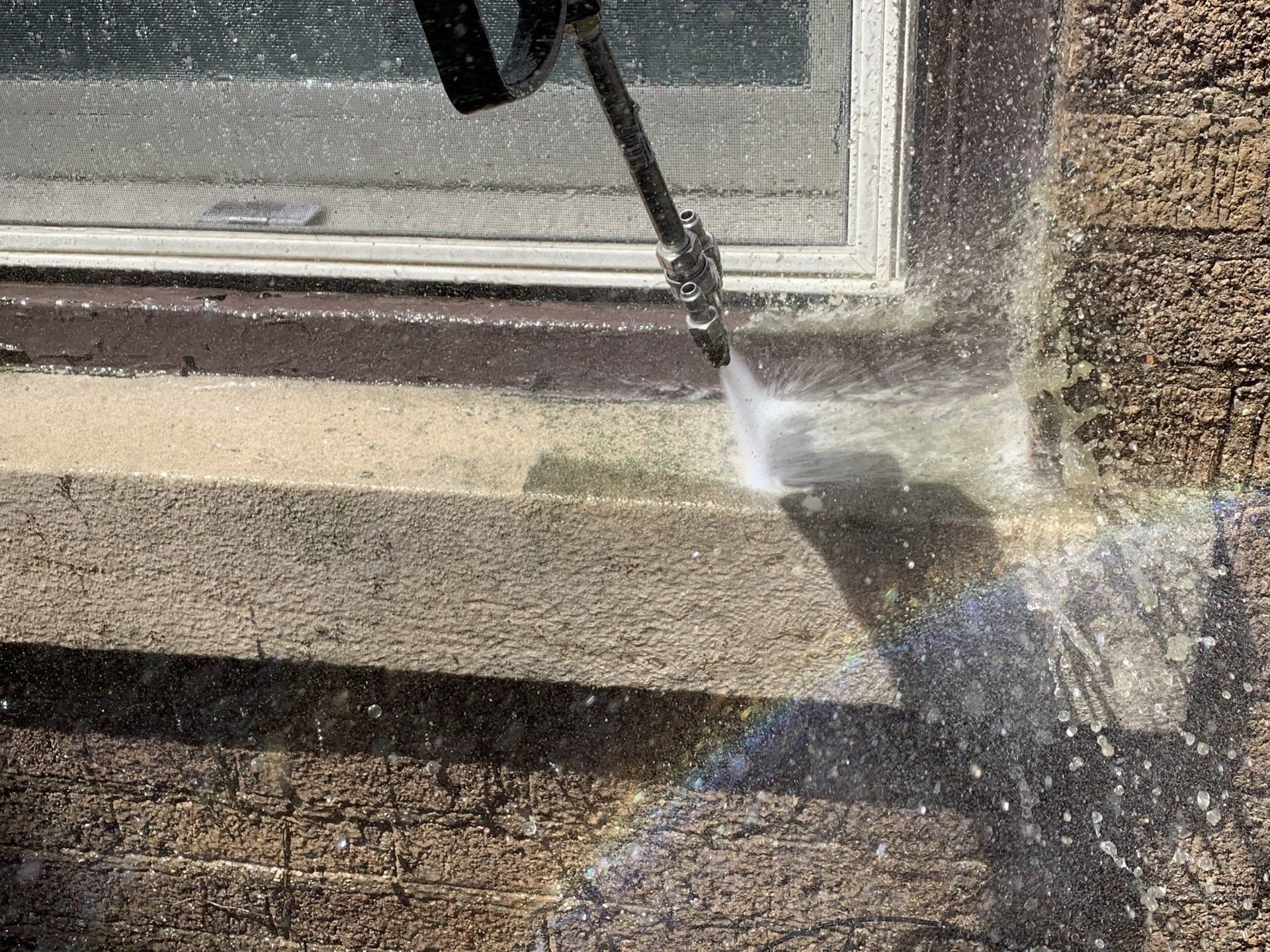 A pressure washer cleans a dirty concrete window sill, revealing a lighter, restored surface beneath the spray.