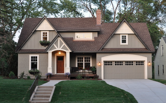 A tan and white two-story suburban house with a brown roof, front porch, and attached garage.