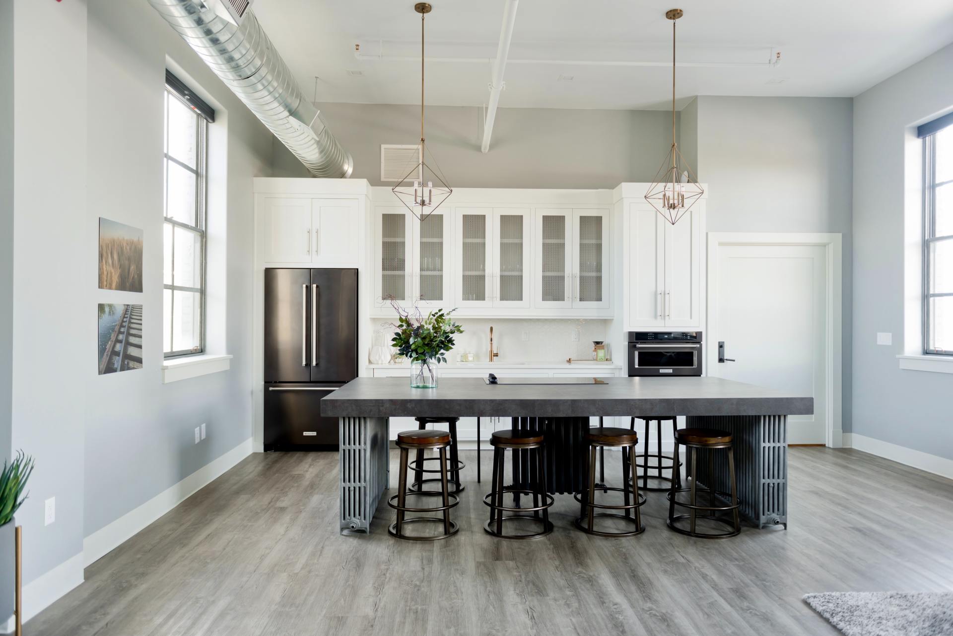 Modern kitchen with white cabinets, a large grey island with four stools, stainless appliances, and light wood flooring.