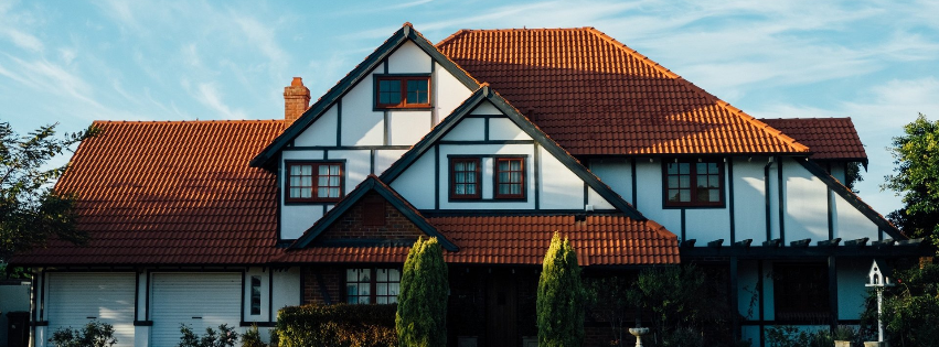 A Tudor-style house with white walls, dark timber framing, and a reddish-brown tiled roof under a clear blue sky.