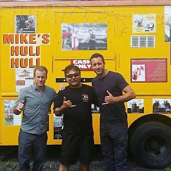 Three men standing in front of a bright yellow food truck. They are making 