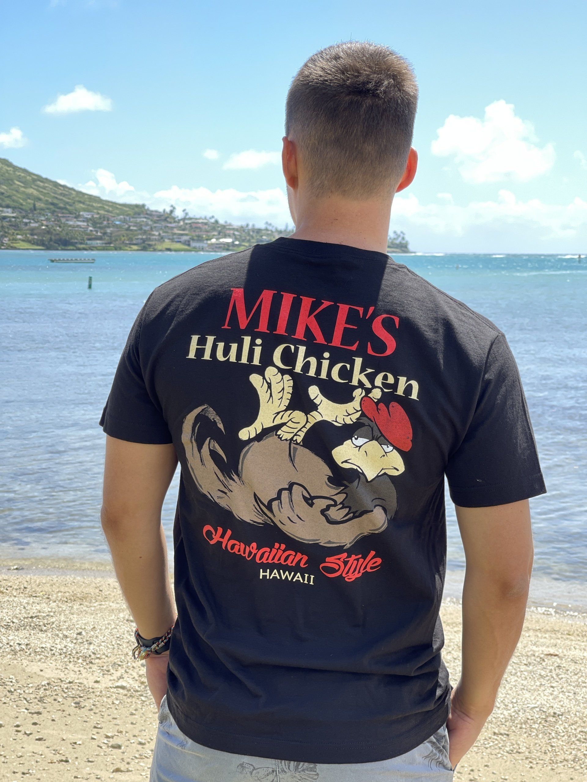 Man standing on a beach wearing a black T-shirt with 