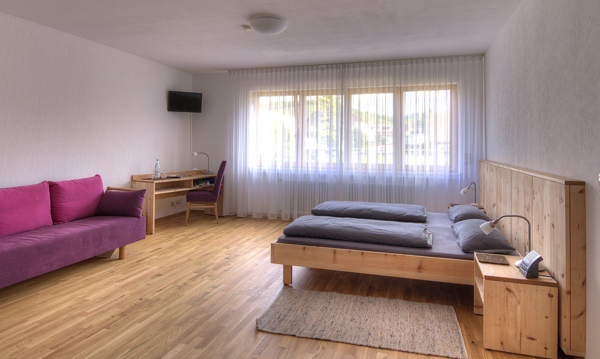 Ein Schlafzimmer mit Bett, Couch, Schreibtisch und Fenster.