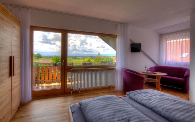 Ein Schlafzimmer mit Bett, Couch, Stühlen und großem Fenster.