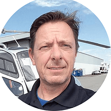 A man in a black shirt is standing in front of a helicopter.