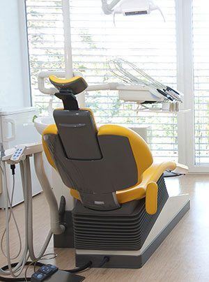 Yellow and gray dental chair in a modern office setting, with equipment and a window in the background.