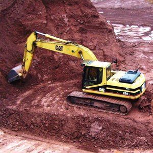 Ein gelber Caterpillar-Bagger gräbt in roter Erde.