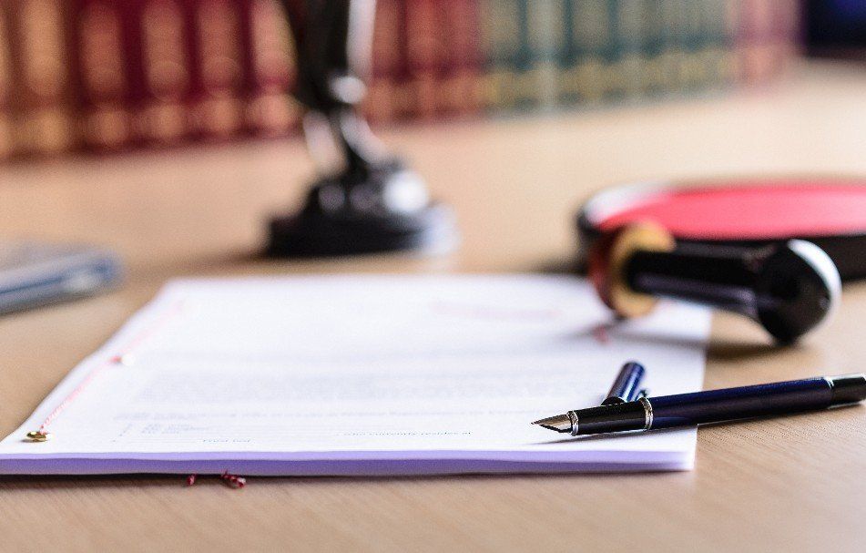 Dokument mit Stift, Stempeln und Büchern im Hintergrund auf einem Holzschreibtisch.