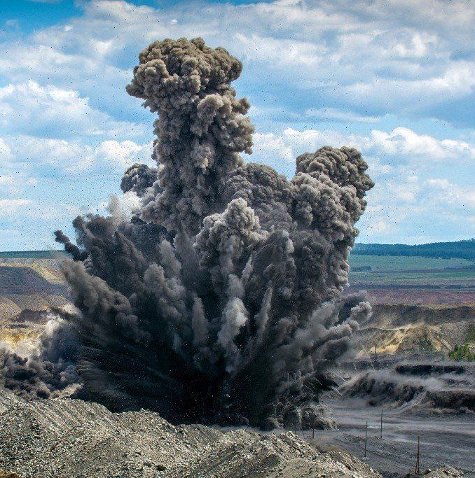 Explosion in einem Steinbruch, bei der eine große Wolke dunklen Rauchs in den Himmel aufsteigt.