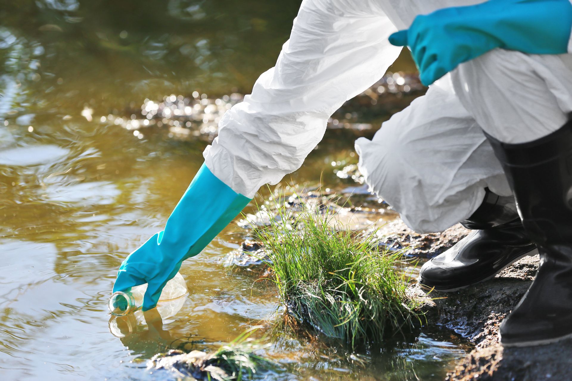 Eine Person in Schutzkleidung entnimmt eine Wasserprobe aus einem verschmutzten Gewässer.