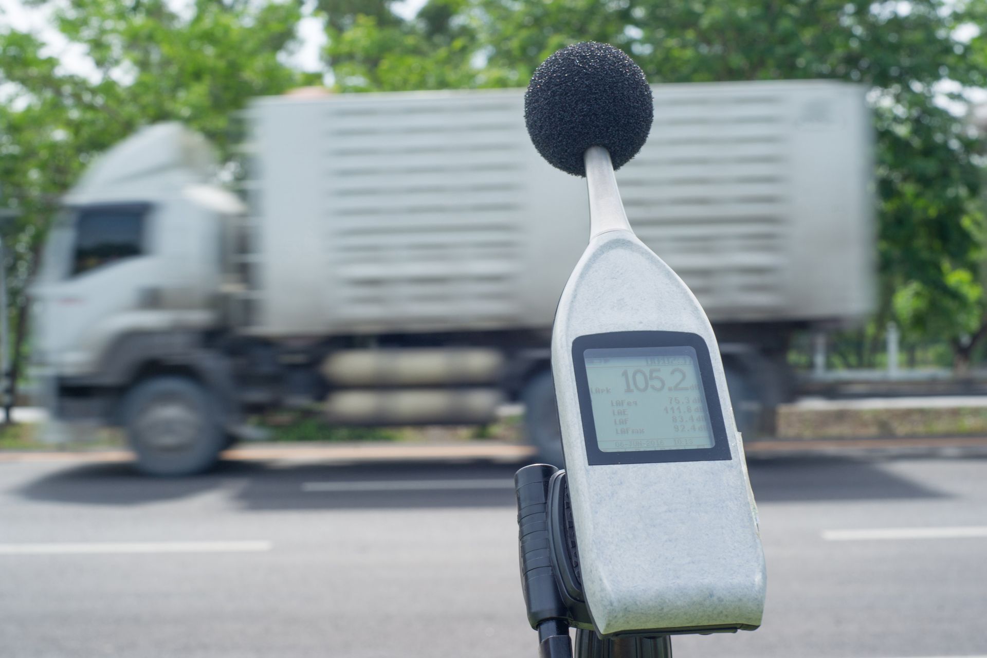 Schallpegelmesser misst Lärm in der Nähe eines verschwommenen LKW auf einer Straße.