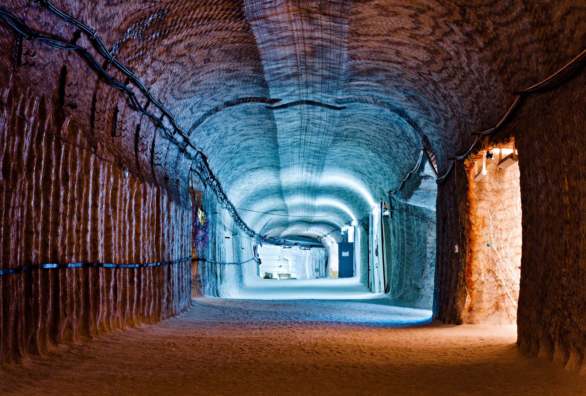 Tunnel mit strukturierten Salzwänden, getaucht in orangefarbenes und blaues Licht.