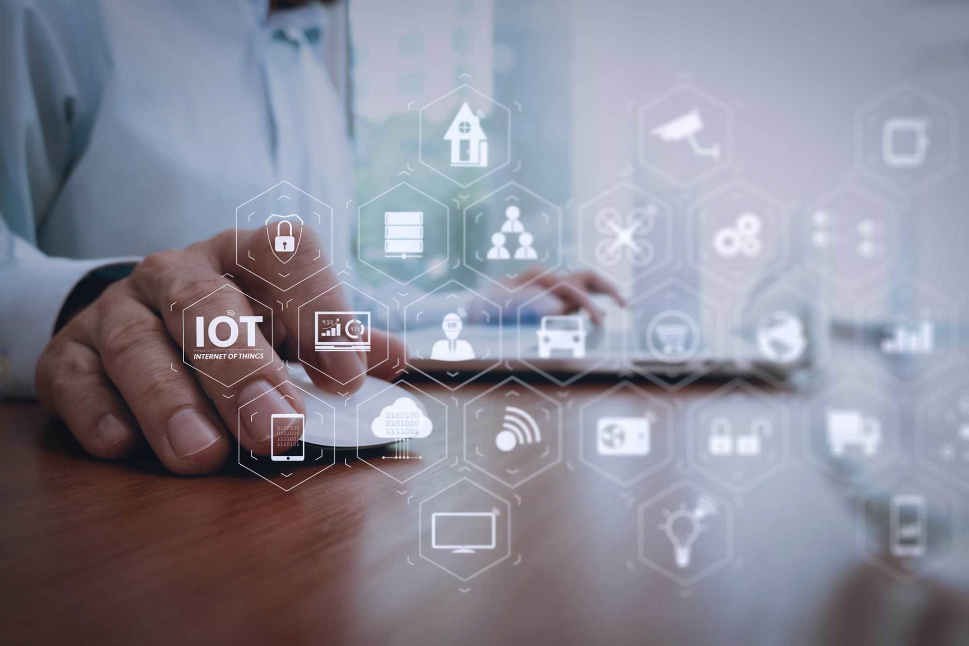 Mano che usa un laptop con icone IoT e di rete fluttuanti sopra una scrivania di legno