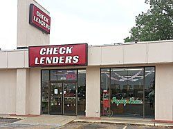 Exterior of a Check Lenders storefront with red signage. Glass doors and windows reflect some of the interior.