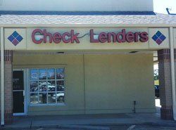 A storefront for Check Lenders with red sign, tan exterior, and a glass door.