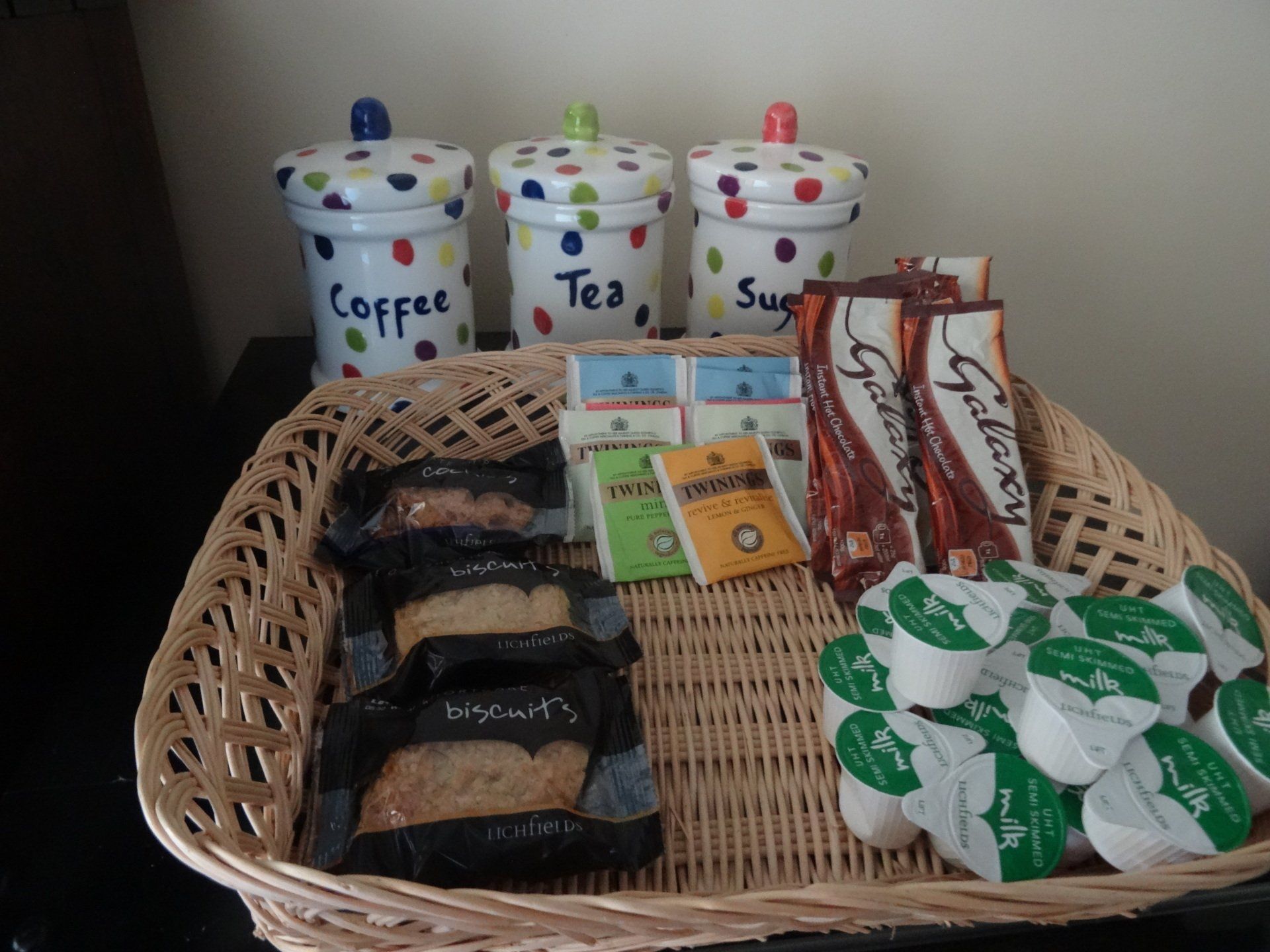 Wicker basket with coffee, tea, sugar canisters, bread and spread packs, and creamer pods.