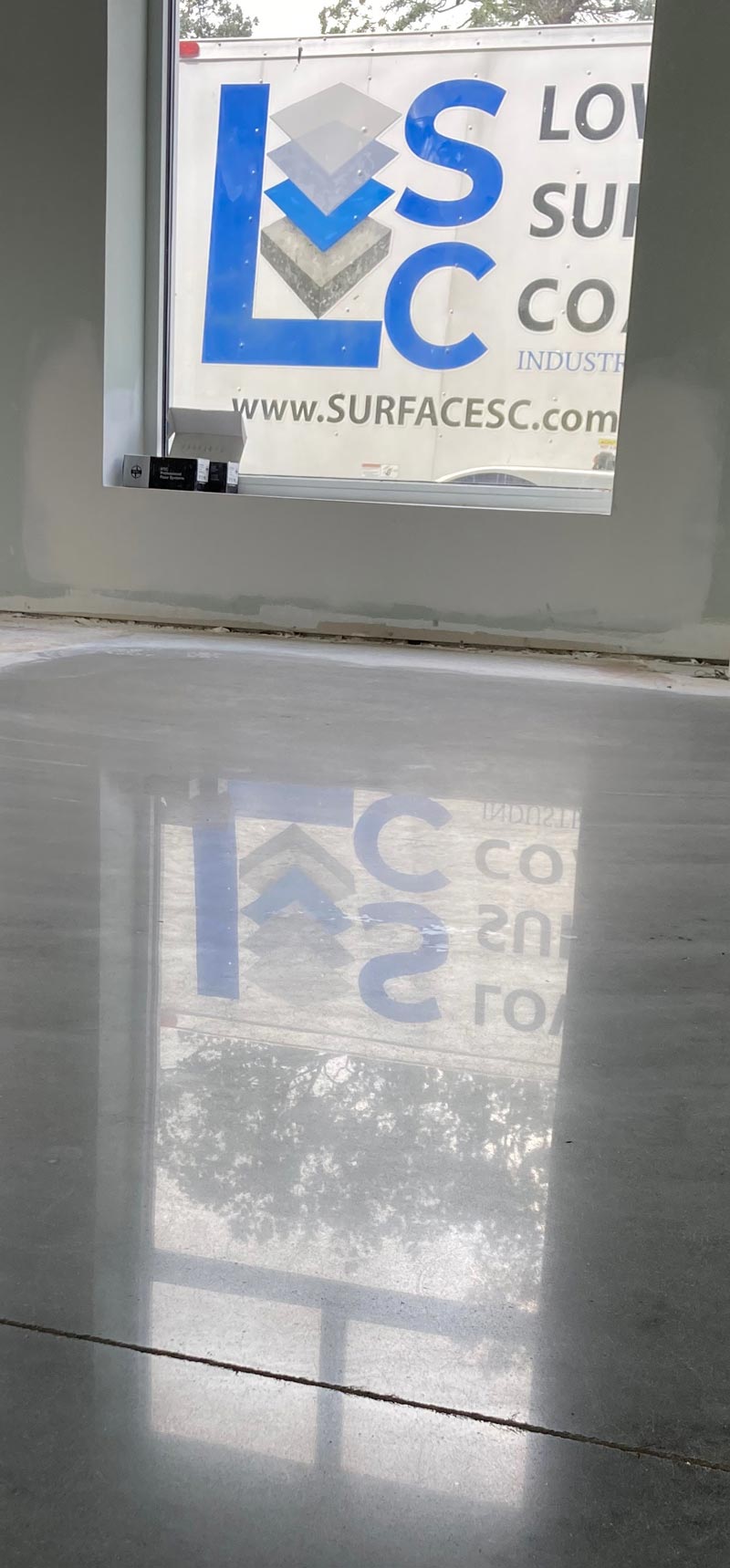 A polished concrete floor reflects a window with the logo 