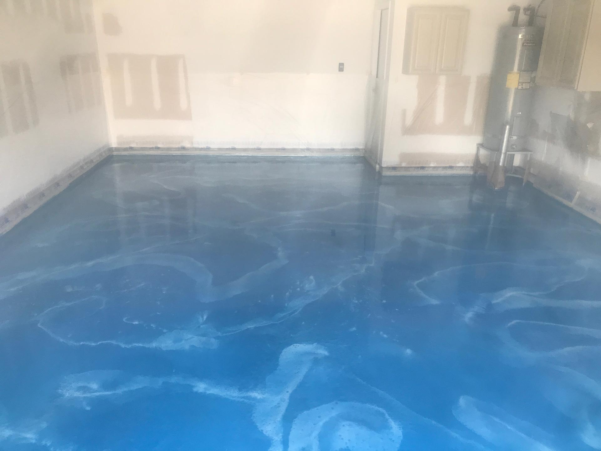 Blue epoxy garage floor with swirled white accents; walls are unfinished.