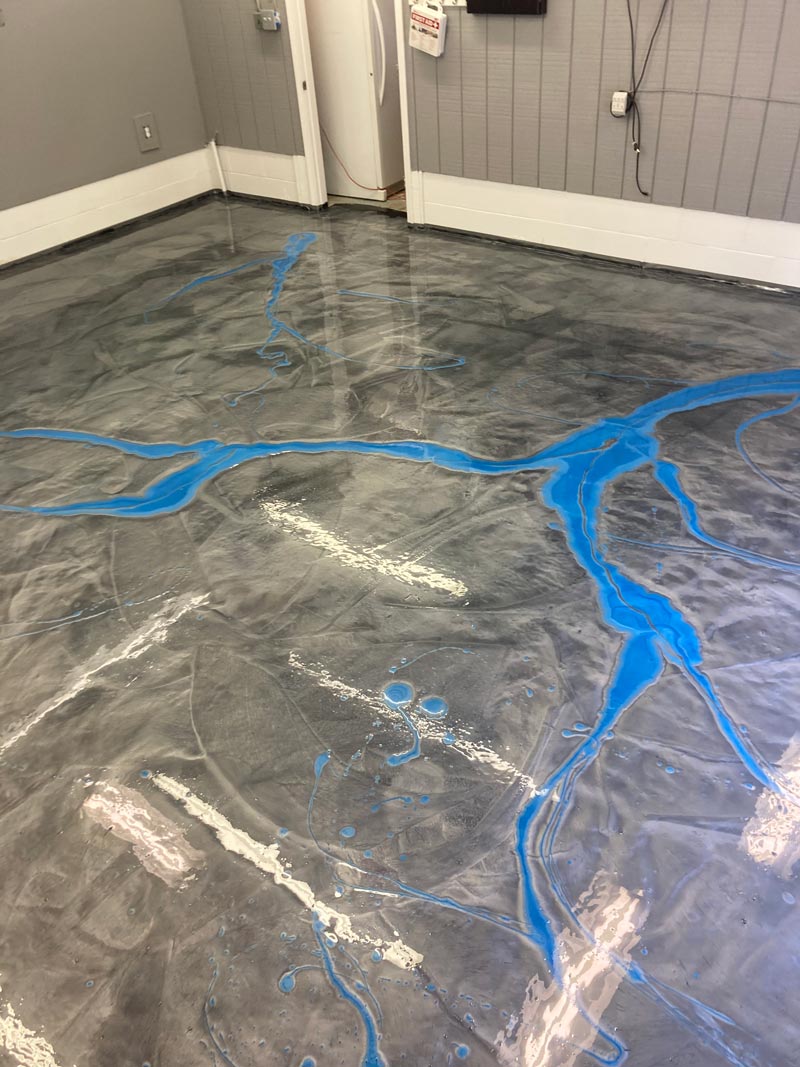 Metallic epoxy floor with gray and blue accents. Blue streams and white splotches decorate the glossy surface in a room.