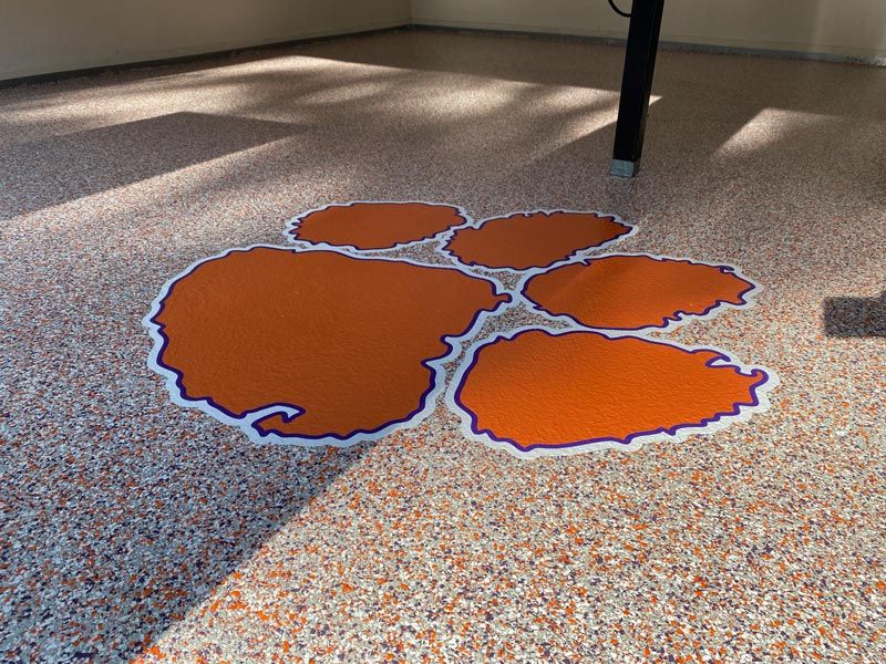 Epoxy flooring with a Clemson paw logo in orange, white, and purple.