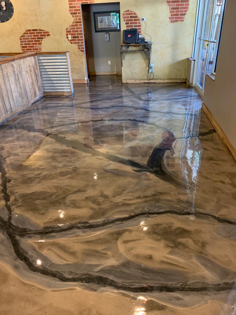 Shiny epoxy floor with dark swirling patterns in a room with brick wall accents and glimpses of a doorway and window.