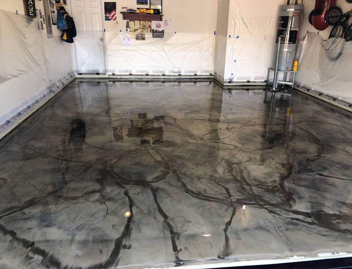 Garage with metallic epoxy floor in shades of gray and black. Walls are white, with tools and equipment visible.