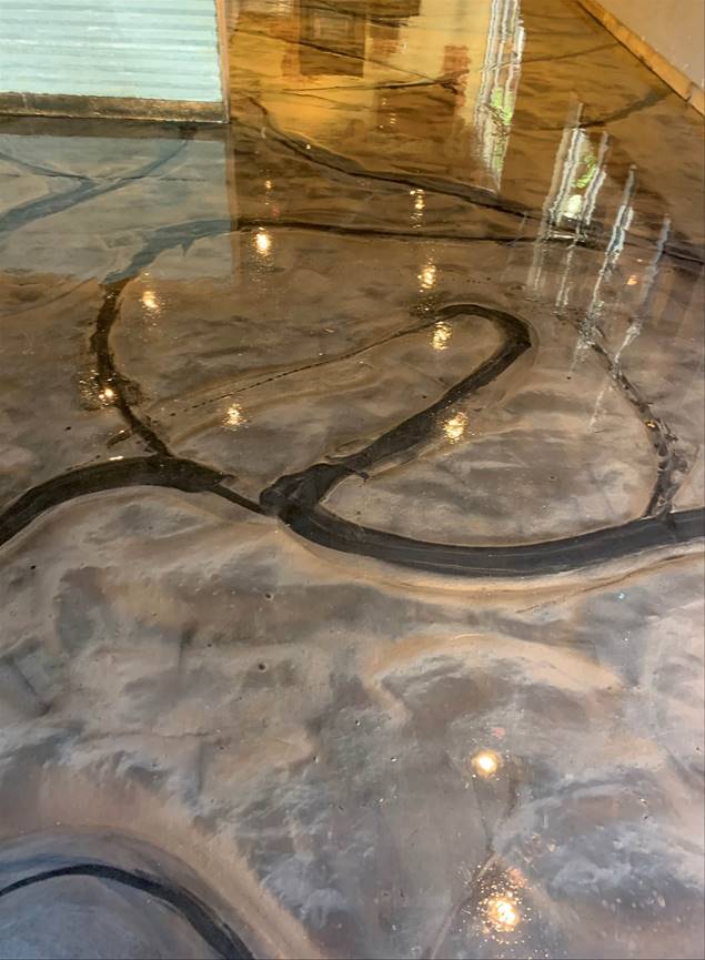 Metallic epoxy floor with black river-like veins on a swirling, tan and grey background. Reflective and glossy.