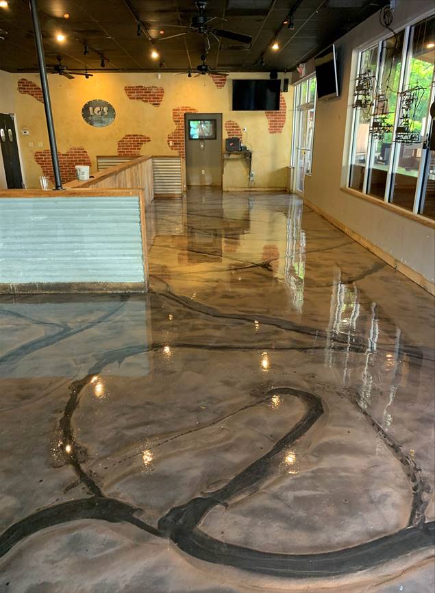 A commercial space with a shiny, epoxy floor featuring black designs. Beige walls and a bar area are visible.