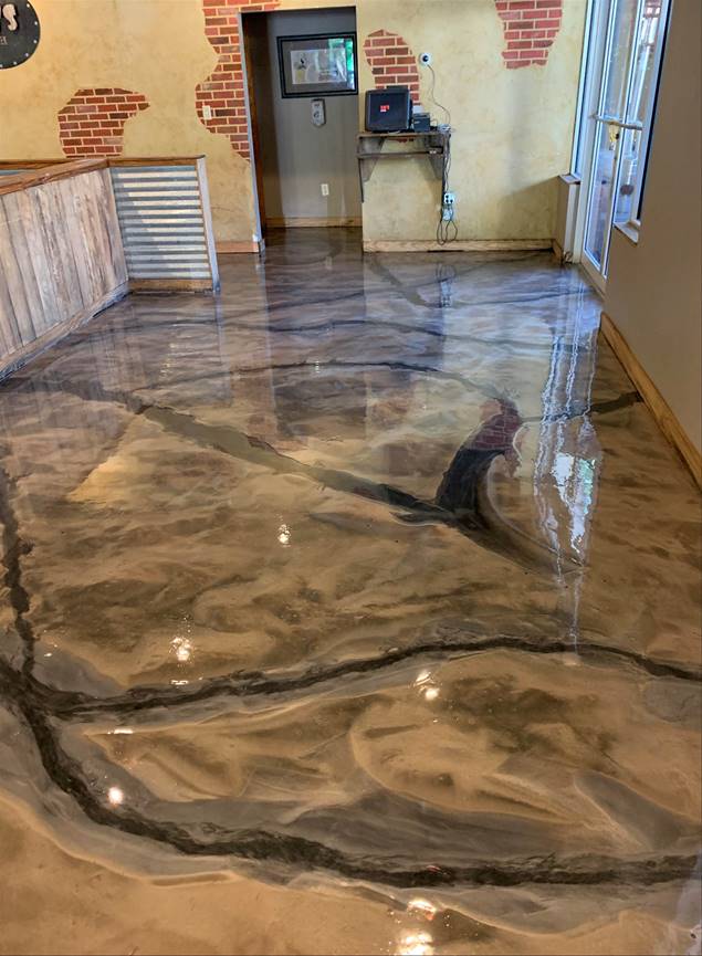 Metallic epoxy flooring in a home, with flowing black and gold patterns. Brick and metal accents on the walls.