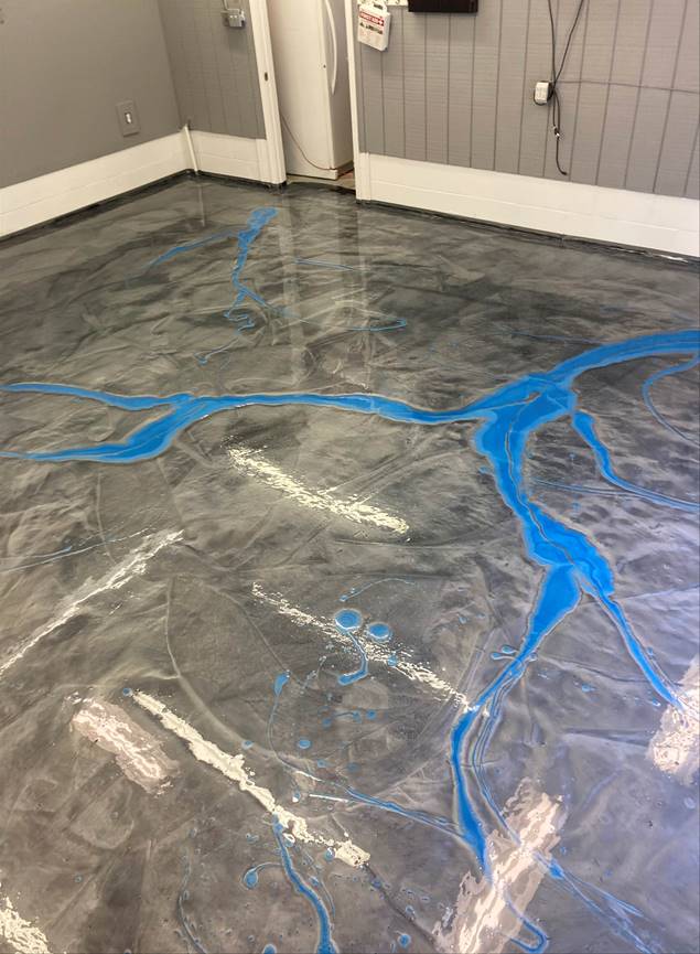 Metallic gray epoxy floor with blue and white accent designs. The room has gray walls and a white door.