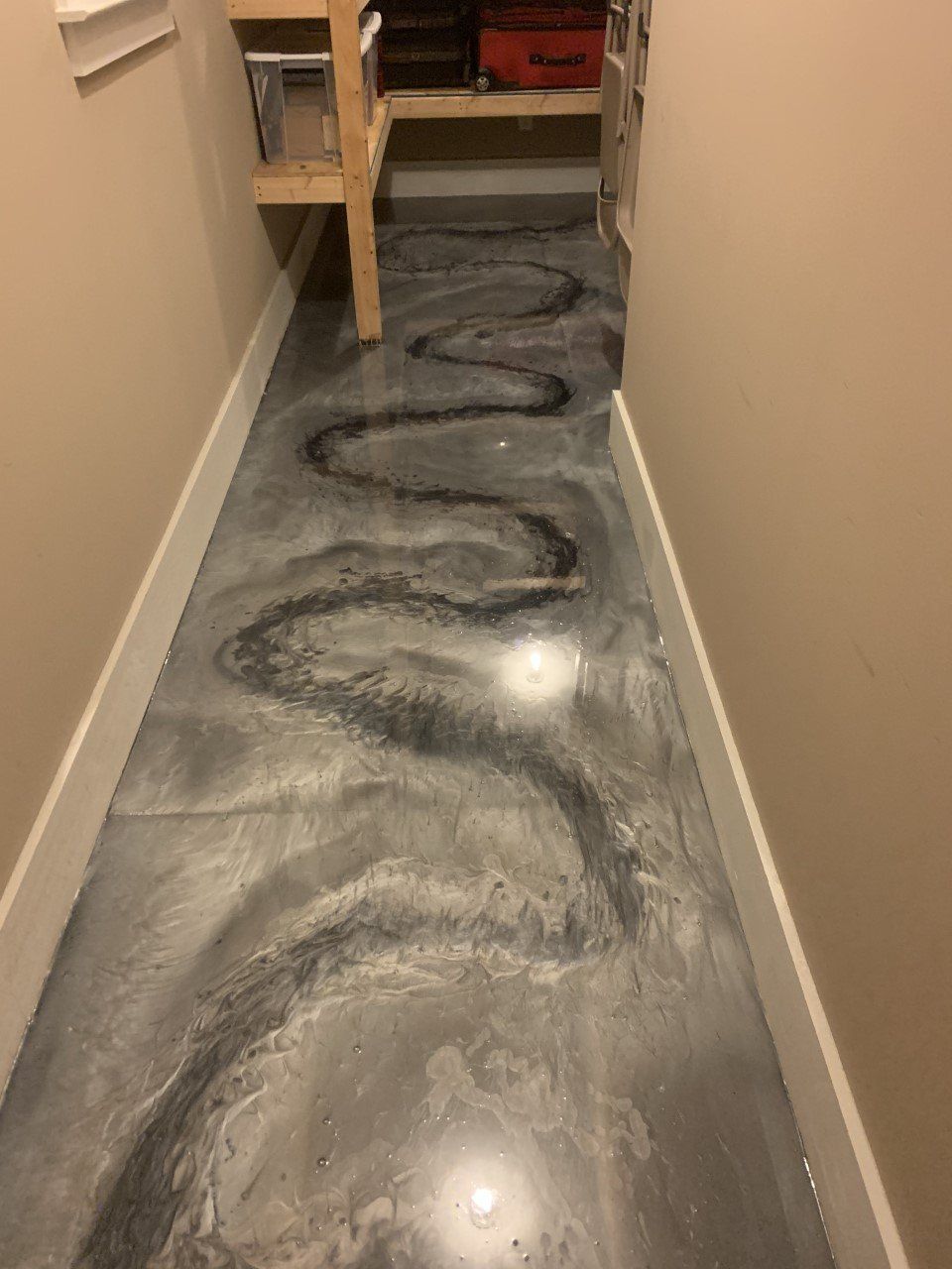 Narrow hallway with metallic gray epoxy floor and a meandering black streak. Beige walls and white trim are present.